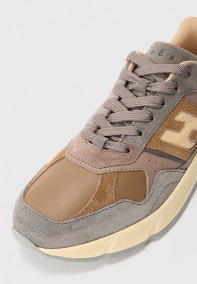 Close-up of brown and gray suede and leather sneaker with beige sole and gray laces on a light background.