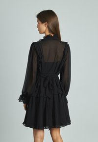 Abito nero con scollatura e maniche arricciate, design a strati e dettaglio con cintura in vita, realizzato in un tessuto trasparente. Mostrato vista posteriore.