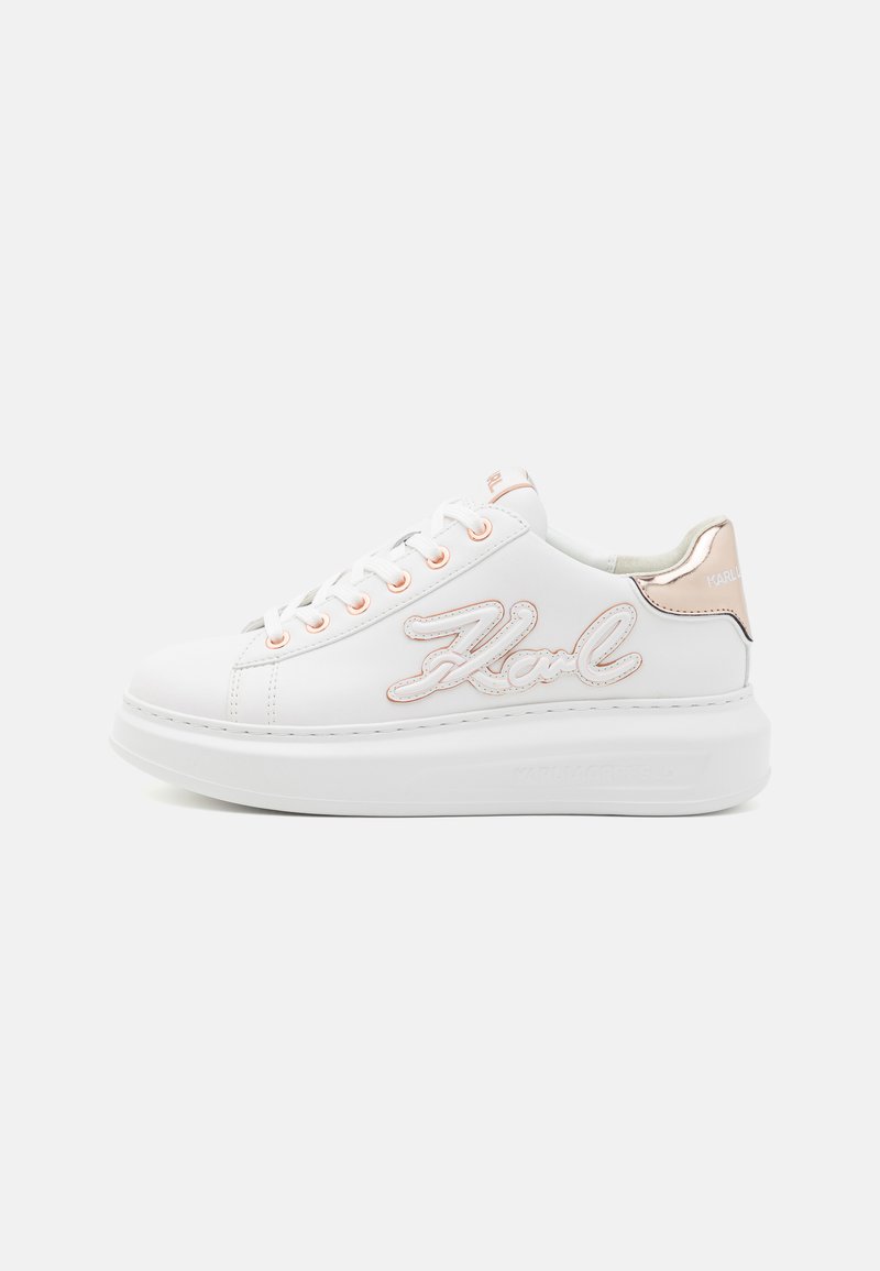 White sneaker with a textured surface, featuring a script logo in pink accents, orange eyelets, and a thick white sole. Metallic heel detail.