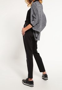 Černé přiléhavé kalhoty s bílými bočními pruhy, zkombinované s volnou, texturovanou šedou vestou. Boty jsou černé s bílým pruhovaným podpatkem.