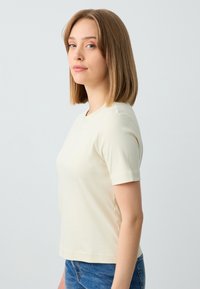 Lichtbeige kortomarm t-shirt van een gladde stof, met een ronde halslijn en een getailleerde pasvorm, gecombineerd met blauwe denim shorts.