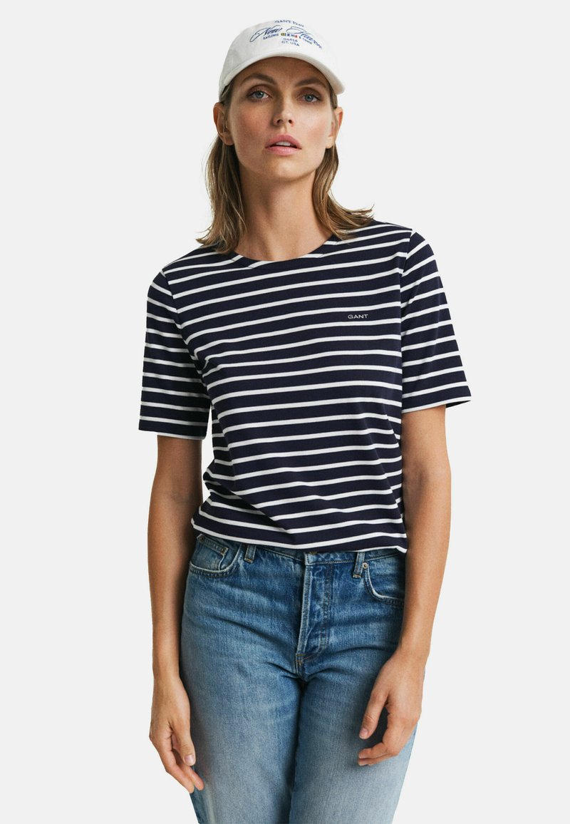 Kortærmet navy- og hvidstribet t-shirt med rund halsudskæring. Har et lille 'GANT' logo på brystet. Bæres med blå jeans.