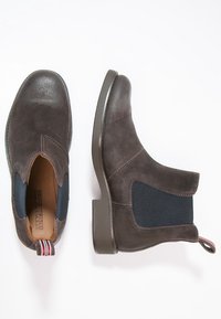 Bruine leren enkellaarsjes met elastische zijkanten, ronde neuzen en een gestreepte trekflap aan de hiel. Platte zolen, subtiele stiksels.