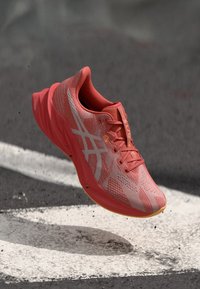 Růžová a oranžová atletická obuv s prodyšnou síťovinou, texturovanými vzory a lehkou podrážkou, která má viditelné šněrování a detaily loga.