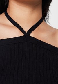 Top senza maniche nero a costine con un design a spalline incrociate, caratterizzato da una finitura tessurizzata e un collo scoperto sulle spalle.