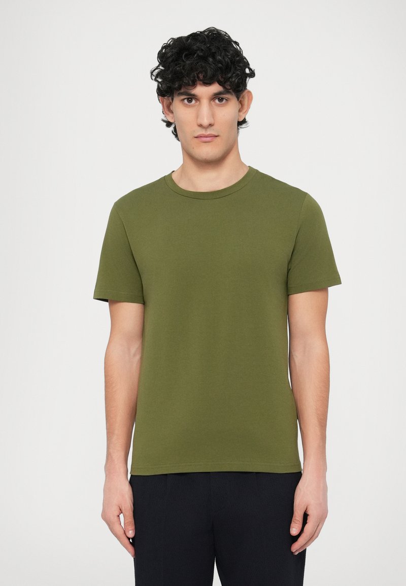 Κοντομάνικη μπλούζα σε ελιά πράσινο χρώμα από βα�μβάκι, με στρογγυλή λαιμόκοψη, λεία υφή και εφαρμοστή γραμμή.