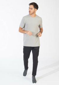 Grå T-shirt med korte ærmer og en tekstureret mønster, parret med sorte tapered bukser og grå træningssko. Står foran en hvid baggrund.