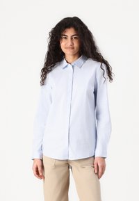 Cămașă cu dungi albastre deschise, cu guler, mâneci lungi și tiv drept. Purtați cu pantaloni bej, având o textură a țesăturii netedă.