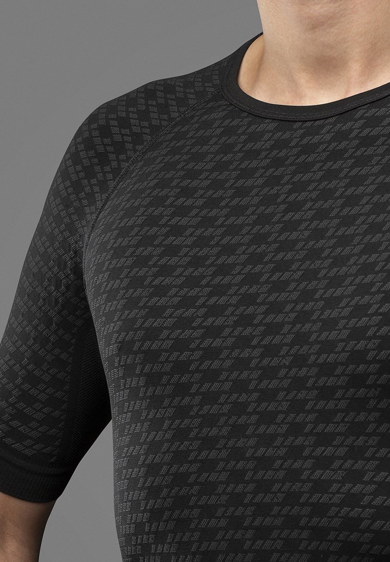 Nahaufnahme einer Person, die ein schwarzes Sportshirt mit einem strukturierten, geometrischen Diamantmuster auf dem Stoff trägt.