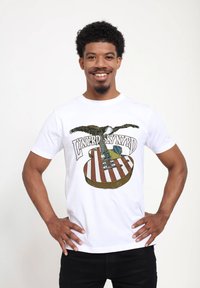 Hvid bomulds T-shirt med grafik af en ørner og en guitar med et amerikansk flag design. Teksten lyder "Lynyrd Skynyrd."