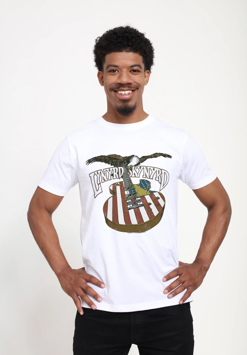 Hvid bomulds T-shirt med grafik af en ørner og en guitar med et amerikansk flag design. Teksten lyder "Lynyrd Skynyrd."