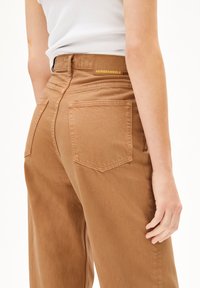 Pantalon taille haute en denim. Doté de deux poches arrière et d'une étiquette de marque au niveau de la taille. Texture lisse.