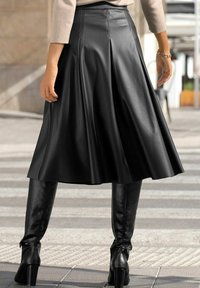 Črna nabrana krila do kolen, izdelana iz gladkega umetnega usnja, v kombinaciji z elegantnimi črnimi škornji do kolen z detajlom s sponko.