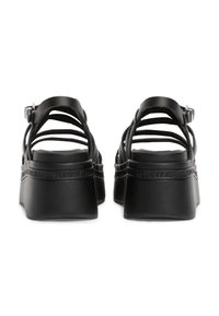 Sandales à plateforme noires avec plusieurs fines lanières, boucle réglable à la cheville, semelle texturée et détail de marque en relief.
