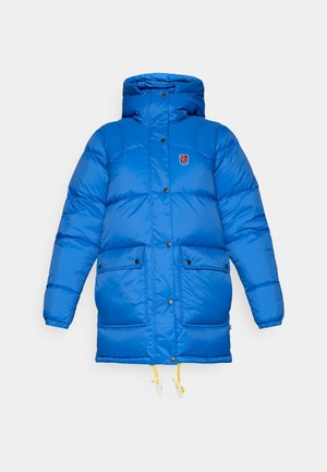 Blauwe pufferjas met een hoge kraag, sluiting met drukknopen aan de voorkant, twee grote zakken en verstelbare gele koordjes aan de onderkant.