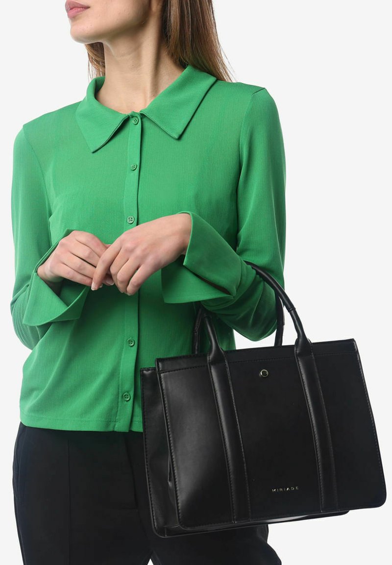 Zwarte leren tote bag met gestructureerd ontwerp, glanzende afwerking en twee handvatten aan de bovenkant. Gepaarde met een groene overhemd met lange mouwen en knopen.