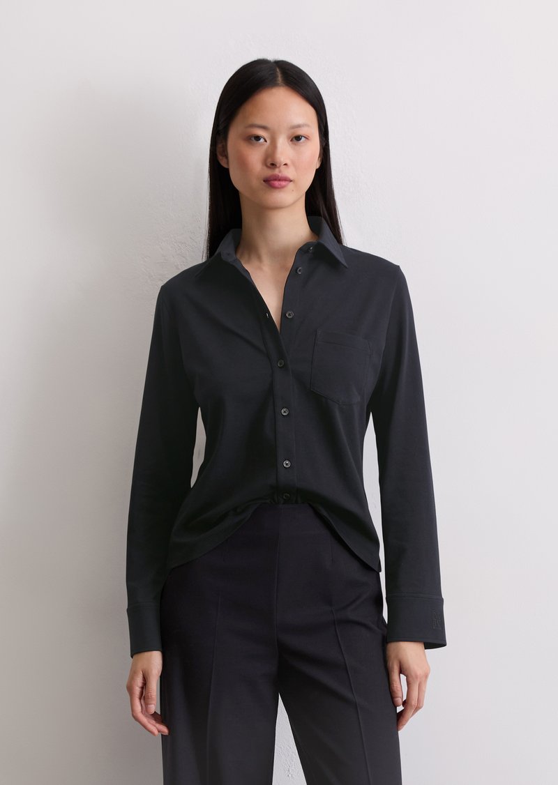 Camicia nera con bottoni, caratterizzata da maniche lunghe, una tasca frontale sul petto e un tessuto morbido. Nota per la sua vestibilità su misura e il colletto a contrasto.
