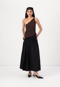 Topul bej, cu un umăr, ajustat, este combinat cu o fustă maxi neagră, cu talie înaltă. Modelul poartă tocuri negre cu spate deschis. Textură fină, design simplu.
