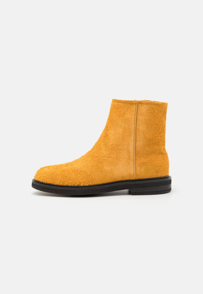 Yellow suede ankle boot with a textured surface, round toe, and a black rubber sole. Features a smooth seam along the back.