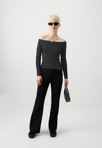 Juoda balta taškelių off-shoulder marškinėliai, ilgos rankovės, raukiniai audiniai, derinami su juodomis plačiomis kelnėmis ir juodais platforminiais batais, laikantis mažą pilką rankinę.