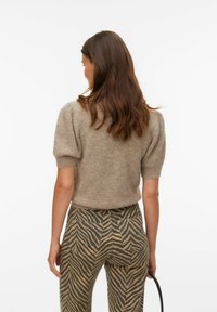 Pull beige en maille à manches courtes avec une finition texturée, associé à un pantalon taille haute rayé marron et beige et un sac à main noir.