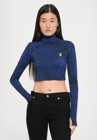 Blue and black patterned, long-sleeve crop top with a high neck. Features a gold logo accent on the chest and a fitted design.
