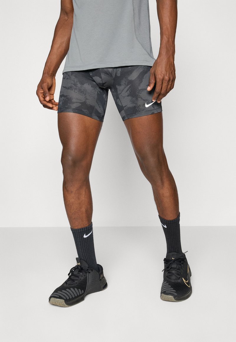 Fekete álcázott sportnadrág, testhezálló fazonnal és fehér Nike logóval, fekete bordázott zoknikkal és fekete sportcipővel párosítva.