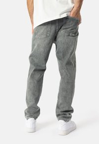 Gai pelēki džinsi ar brīvu piegriezumu, ar diviem aizmugures kabatām un smalku tekstūru. Stilizēti ar baltām sporta apaviem.