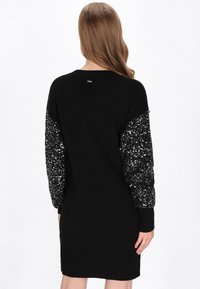 Zwarte sweaterjurk met lange, gepailletten mouwen, geribbelde manchetten en zoom. Glad fabric met een aansluitende pasvorm, met een detail op de rug bij de hals.