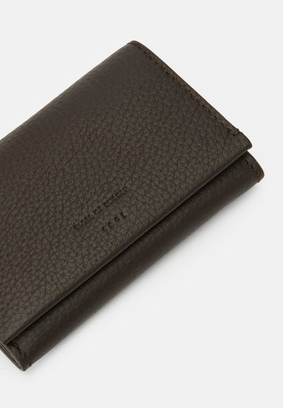 Portafoglio in pelle textured marrone scuro con nome del brand in rilievo e cuciture lungo i bordi, chiuso e angolato su uno sfondo bianco.