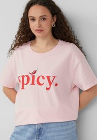 Lichtroze katoenen t-shirt met vet rood tekst die "spicy" zegt, met een kleine chilipeper boven de letter 'i'. Korte mouwen, ontspannen pasvorm.