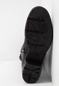 Bota de cuero negro con suela texturizada, que cuenta con una cremallera en el costado y un logo grabado. Talla 37 marcada en la suela.