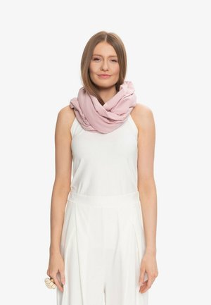 Młoda kobieta ubrana w bezrękawnik biały top i spodnie, z jasnoróżowym szalikiem owiniętym wokół szyi na białym tle.