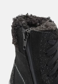 Bota de ante negra con un cuello texturizado y peludo, cierre de cremallera y cordones negros. Acabada con sutiles detalles brillantes a lo largo de los lados.