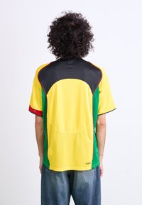 Yellow and green sports jersey with black mesh detailing, short sleeves, and red accents. Features a round neckline and soft fabric texture.