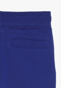Los pantalones de chándal de algodón azul presentan una cinturilla acanalada y un pequeño bolsillo trasero con una abertura cosida. Tienen una textura suave y un acabado liso.