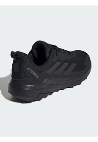Chaussures de sport noires avec une tige en mesh texturé, un talon renforcé et un design à trois bandes. Comprend un col rembourré et une semelle extérieure robuste.