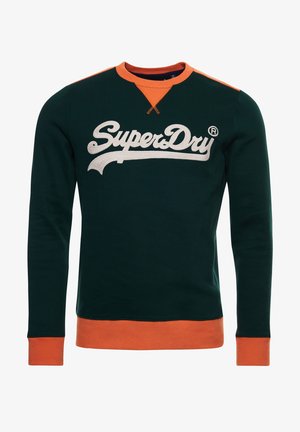 Ciemnozielona bluza z pomarańczowym kołnierzem, mankietami i dołem, z dużym białym napisem "SuperDry" na piersi.