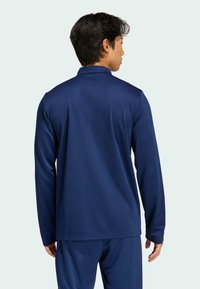 Μακρυμάνικη πόλο μπλούζα σε ναυτικό μπλε χρώμα με απαλό, υφασμάτινο υλικό και γιακά. Διαθέτει ευθεία ραφή στο κάτω μέρος και διακριτά δομημένους ώμους.