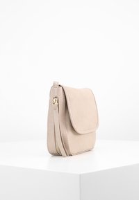 Beżowa skórzana torba na ramię z klapką, zapinaną na suwak kieszenią boczną oraz gładką fakturą. Kompaktowy, prostokątny kształt.