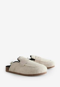 Filzhausschuhe in Creme mit schwarzem Innenfutter, ausgestattet mit einem hellbraunen Riemen, runder Form und einer naturfarbenen Sohle. Weiche Textur und lässiges Design.