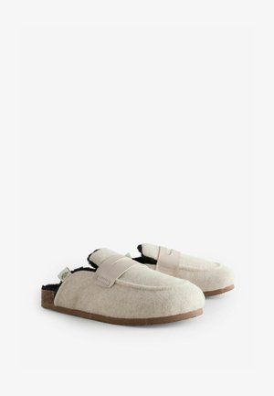 Filzhausschuhe in Creme mit schwarzem Innenfutter, ausgestattet mit einem hellbraunen Riemen, runder Form und einer naturfarbenen Sohle. Weiche Textur und lässiges Design.