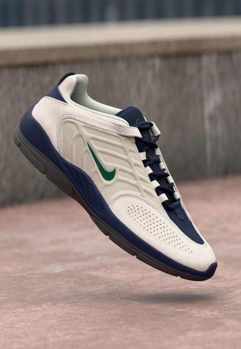 Hvite og marineblå sneakers med teksturert overdel, grønn swoosh og perforerte detaljer. Rund tå og polstret såle. Snøresystem.