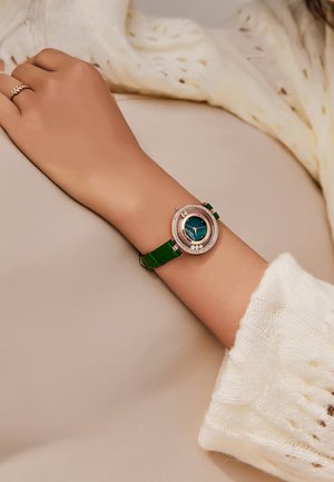 Reloj de pulsera redondo con correa de cuero verde y un dial azul, enmarcado por un bisel de oro rosa texturizado adornado con pequeñas gemas.
