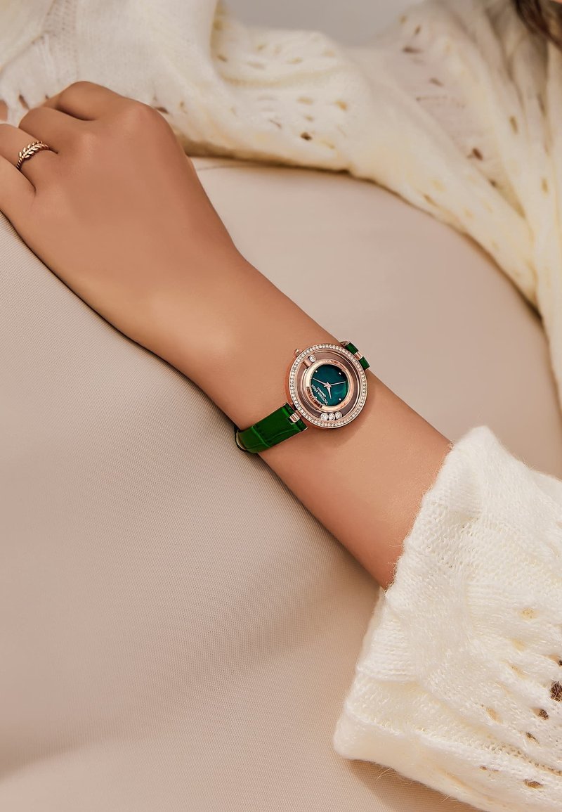 Reloj de pulsera redondo con correa de cuero verde y un dial azul, enmarcado por un bisel de oro rosa texturizado adornado con pequeñas gemas.