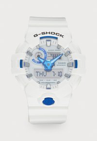 Montre G-Shock blanche avec des accents bleus, affichage numérique et analogique, bouton poussoir texturé bleu, caractéristiques résistantes aux chocs et étanchéité.