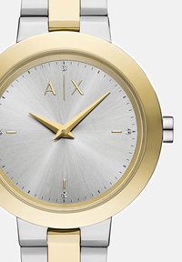 Sidabrinė ir auksinė nerūdijančio plieno laikrodis su šlifuotu sidabro ciferblatu, auksiniais valandų žymekliais ir dviem akcentiniais deimantais 12 ir 6 valandų padėtyse.