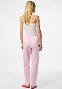 Lichtroze sweatpants gemaakt van zachte stof met een elastische tailleband, gecombineerd met een witte geribbelde tanktop en roze teenslippers.
