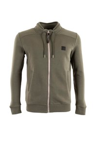 Giacca zip a olive con colletto alto, tasche frontali, corde di regolazione, polsini e orlo a costine, e una piccola toppa nera sul petto.