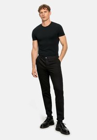 Zwarte, aansluitende t-shirt gecombineerd met zwarte slim-fit broeken. Het model draagt zwarte veterschoenen, die een strak, minimalistisch ontwerp uitstralen.